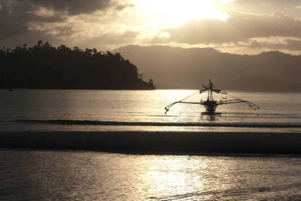 Sunset silhouette of a traditional outrigger boat on Pagdanan Bay at Port Barton, Palawan.