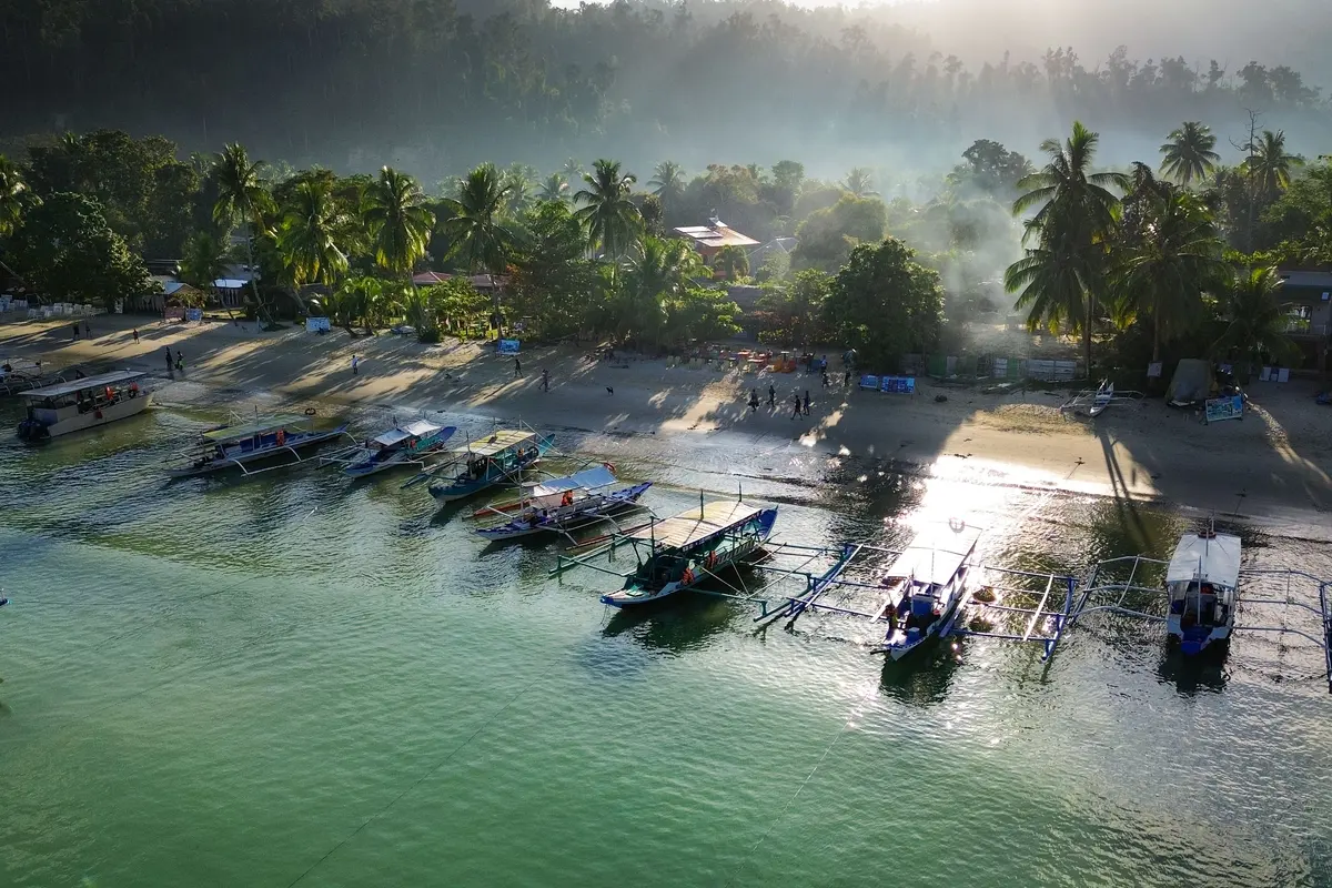 Traditional outrigger boats lined up beside a sandy beach in San Vicente, Palawan.