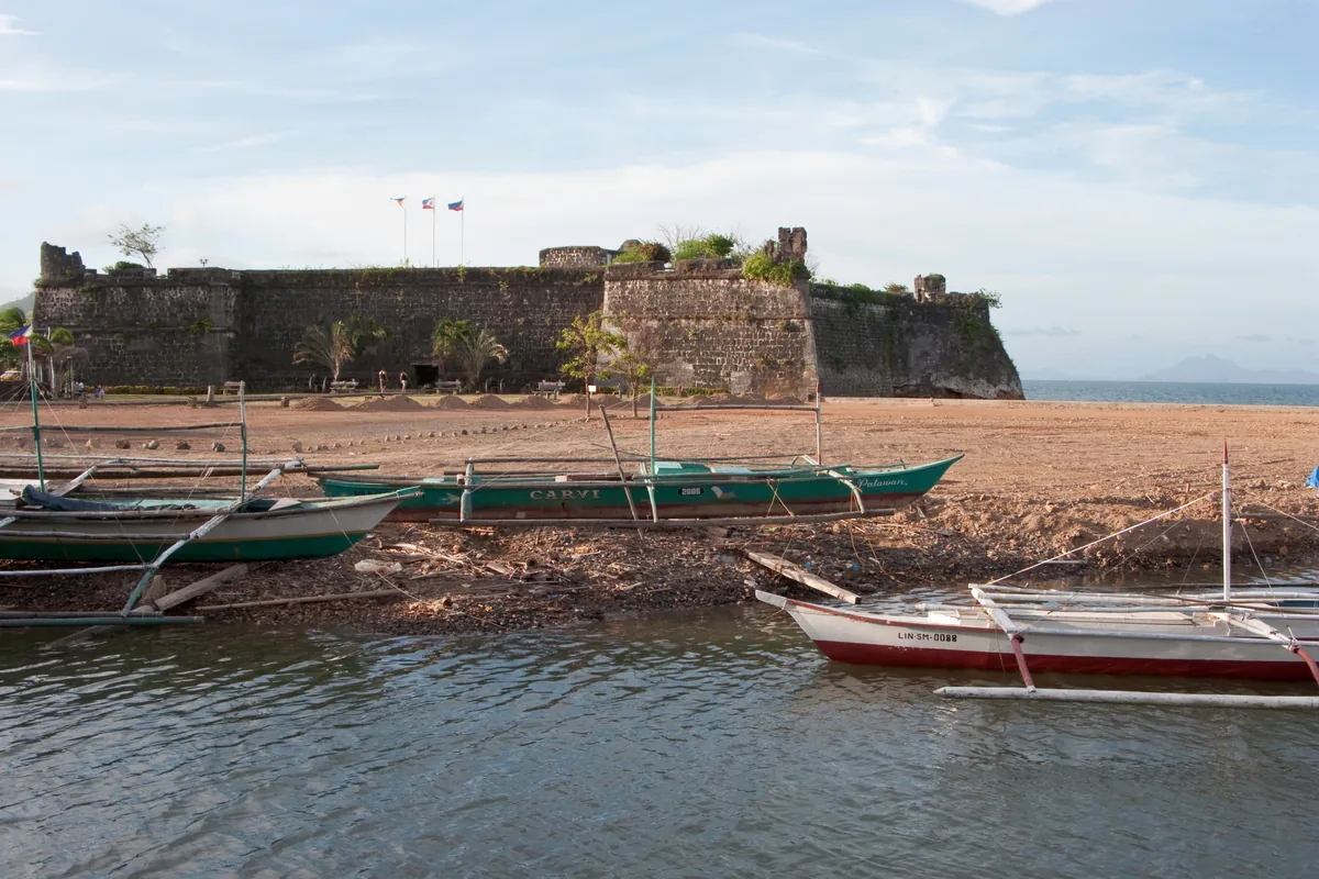 The stone walls and bastions of Fuerza de Santa Isabel with outrigger boats on the shore at Taytay, Palawan.