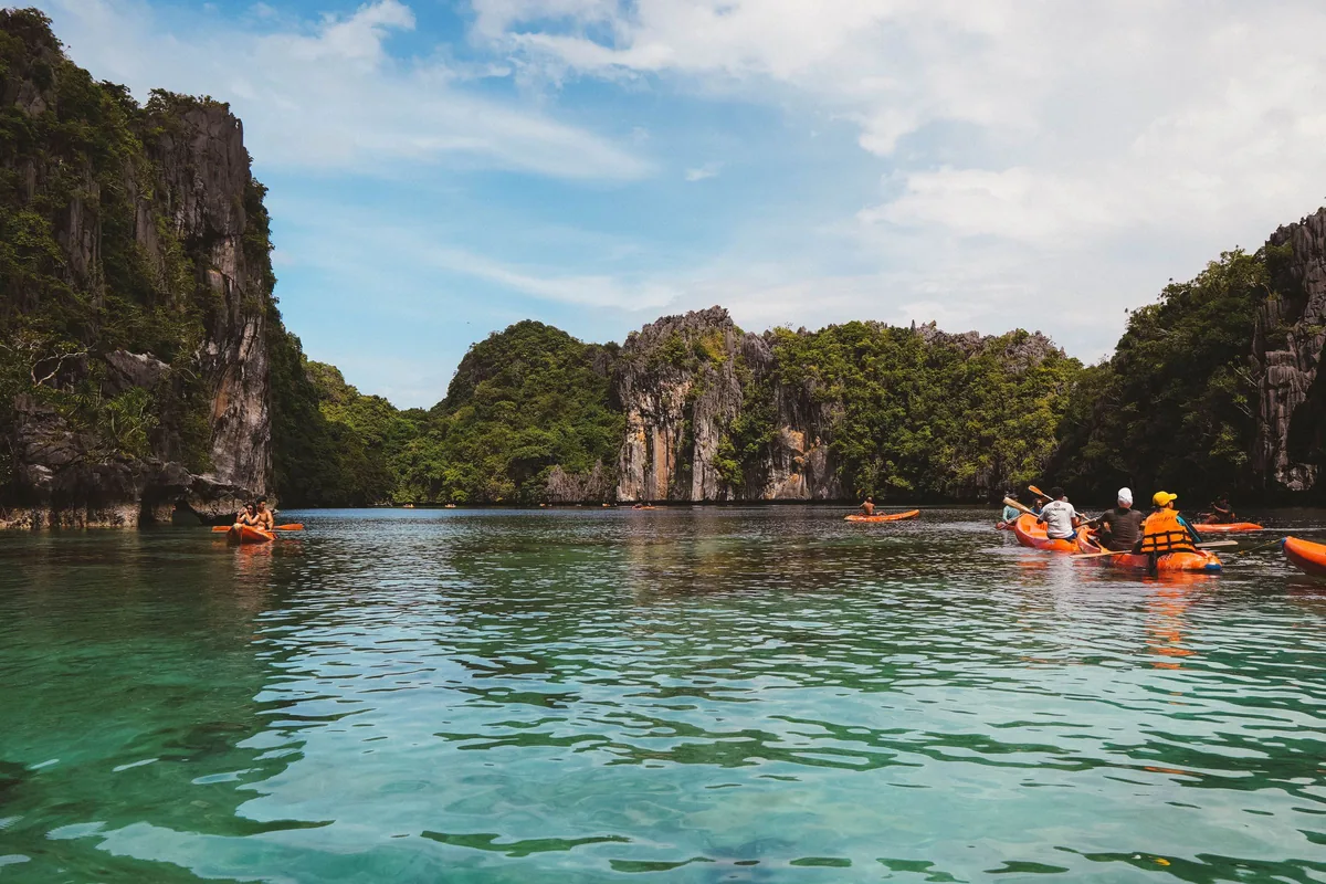 Kayakers below limestone cliffs on the turquoise water of Bacuit Bay, El Nido, Palawan, Philippines.