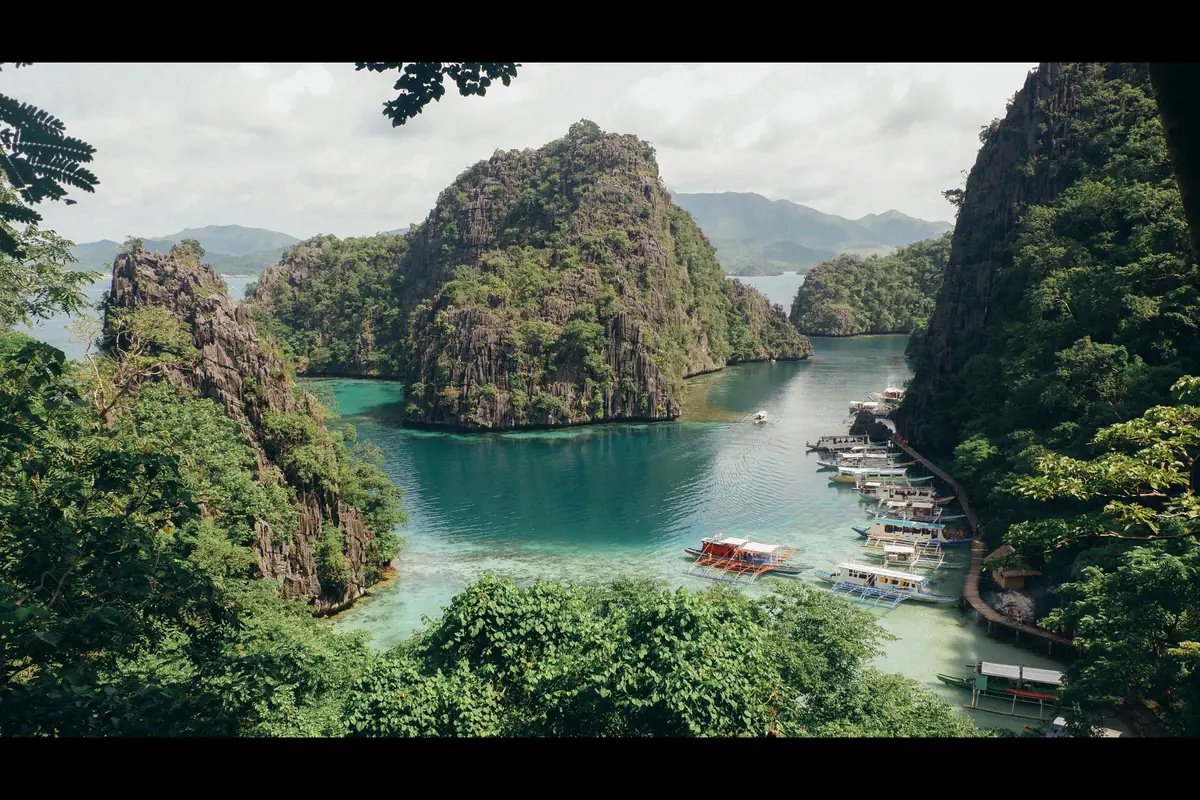 Limestone karst islands and outrigger boats on turquoise water at Coron Bay, Palawan, Philippines.