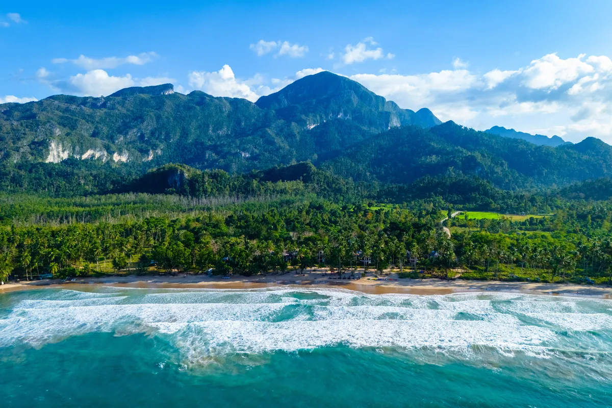 Aerial view of a tropical beach and lush forested mountains along the Palawan coast, Philippines.